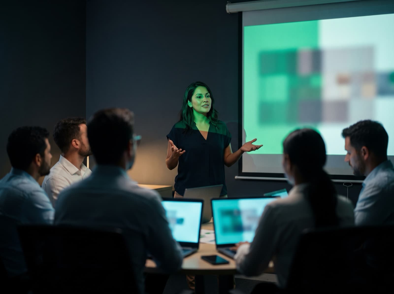 Professional presenting to their team, standing in front of a screen that bathes the room in cyan light